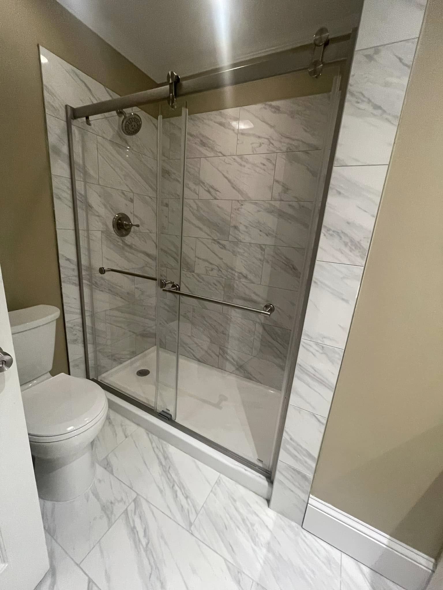 Modern bathroom with white marble-patterned tile, a glass-enclosed shower with sliding doors, and a white toilet.