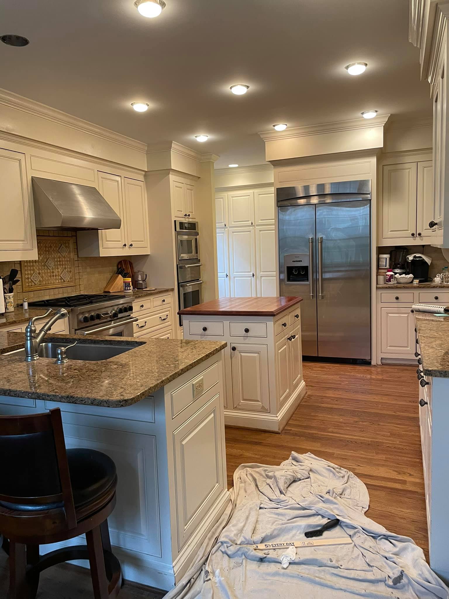 Spacious kitchen with white cabinets, stainless steel appliances, granite countertops, a center island, and a cloth with a tool on the wooden floor.